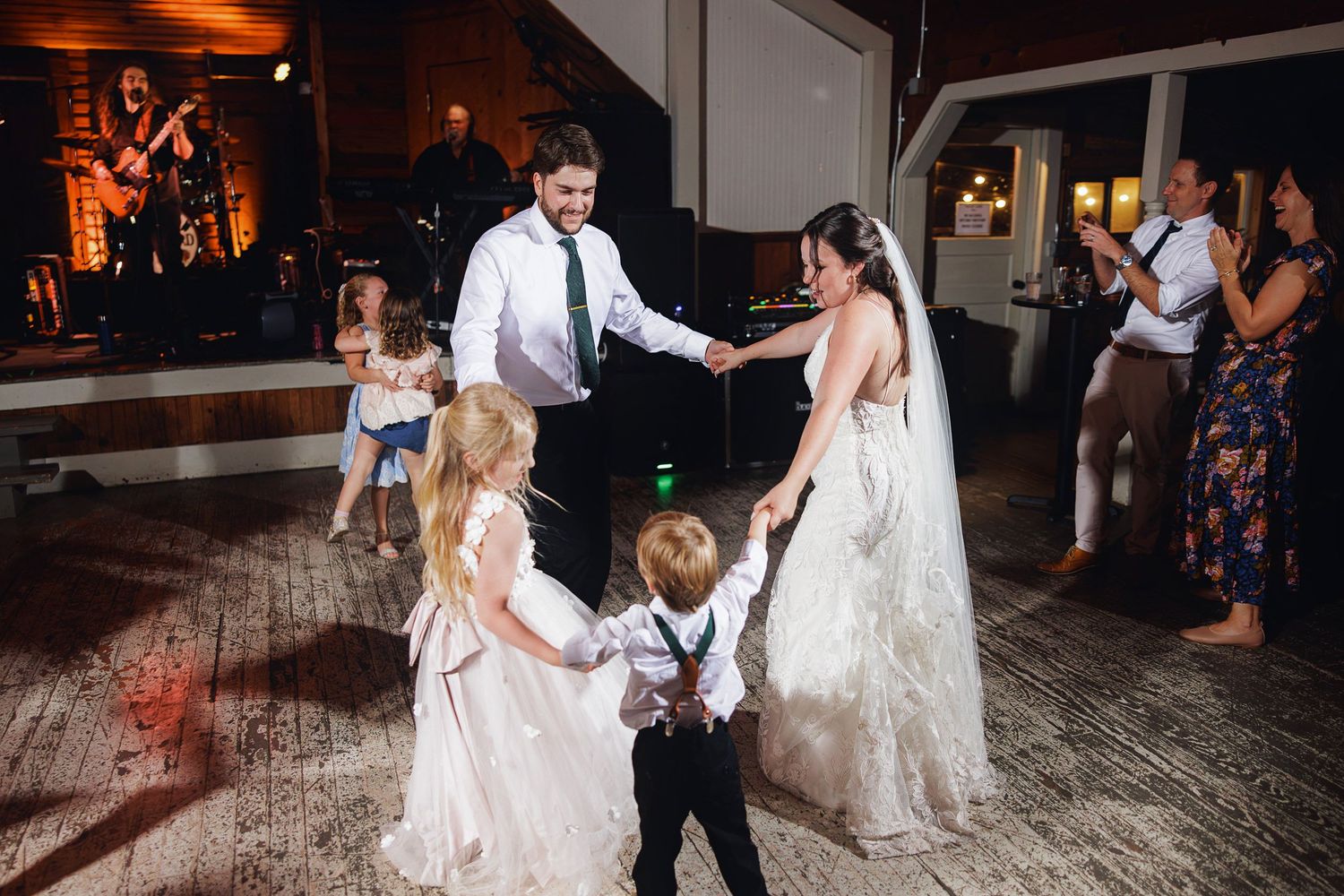 Bride and groom dancing with children on wedding reception dance floor while guests celebrate in background.