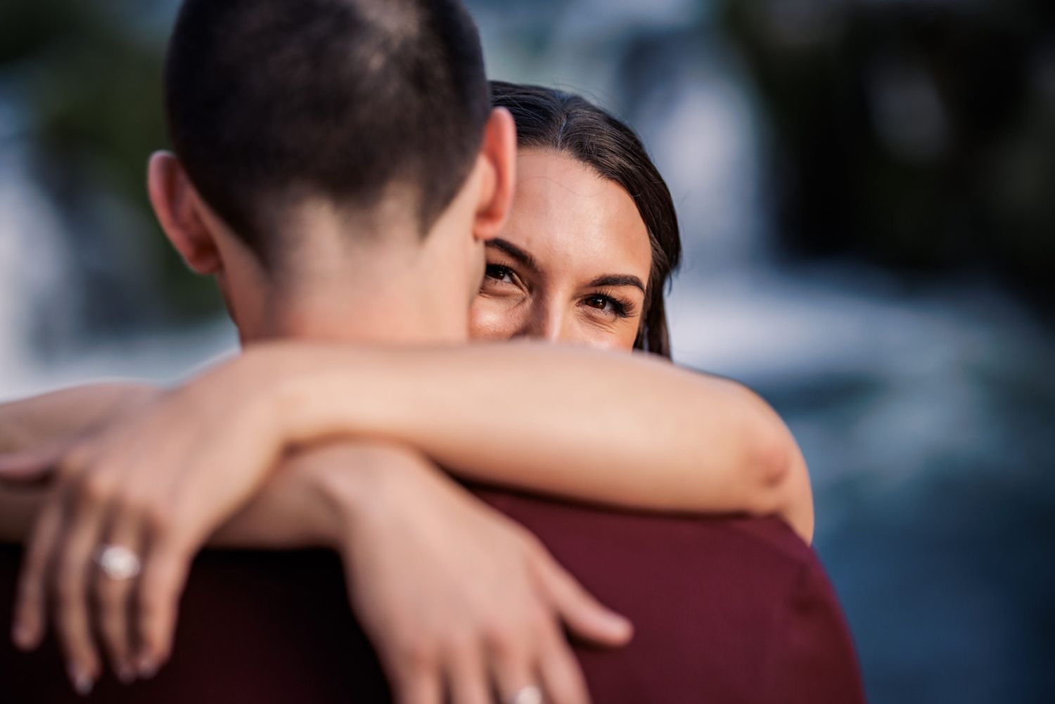 An intimate embrace captured in soft focus with one person's face visible over another's shoulder.
