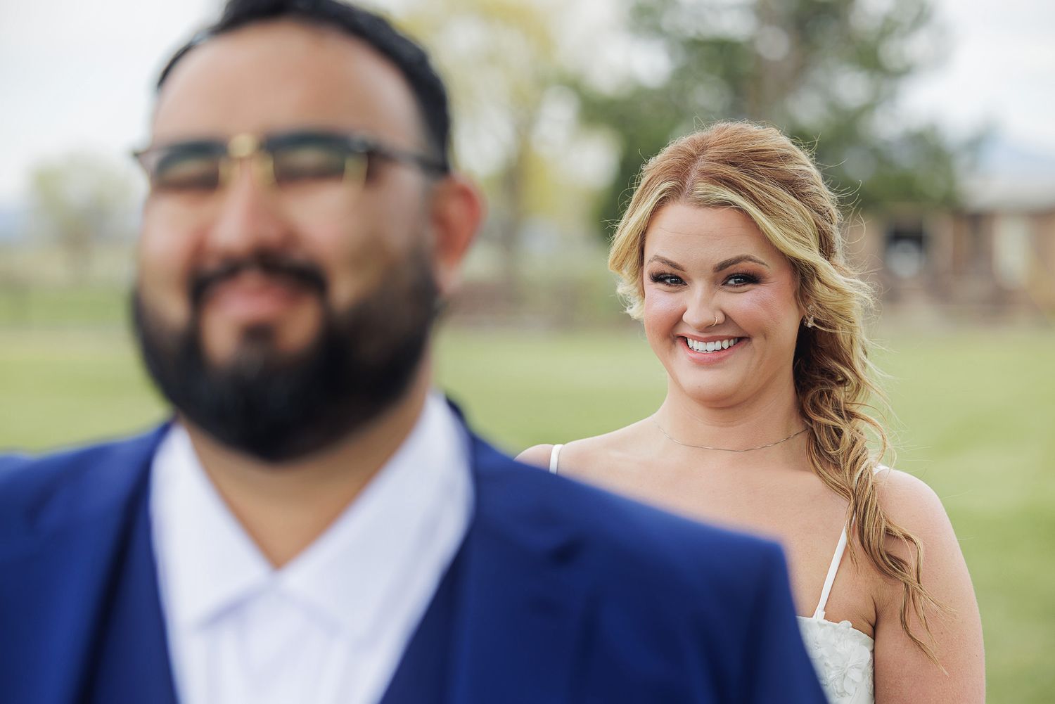 Bride smiling joyfully at groom in blue suit during outdoor wedding first look ceremony.