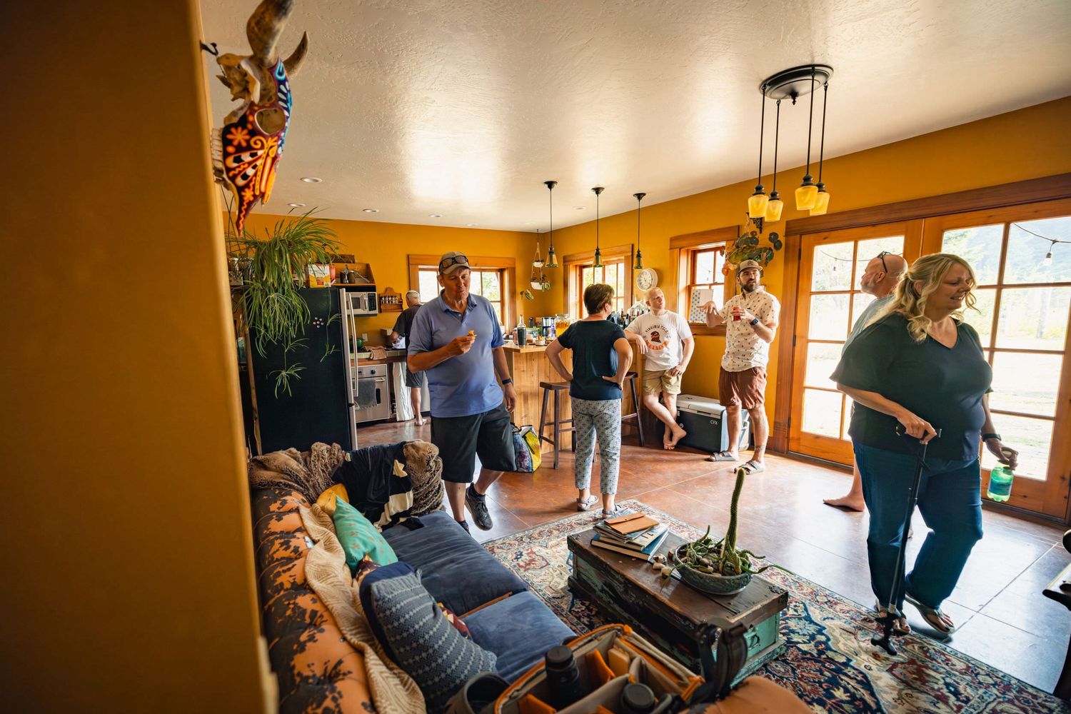 People gather in a cozy living room with warm lighting during a casual indoor gathering or house party.