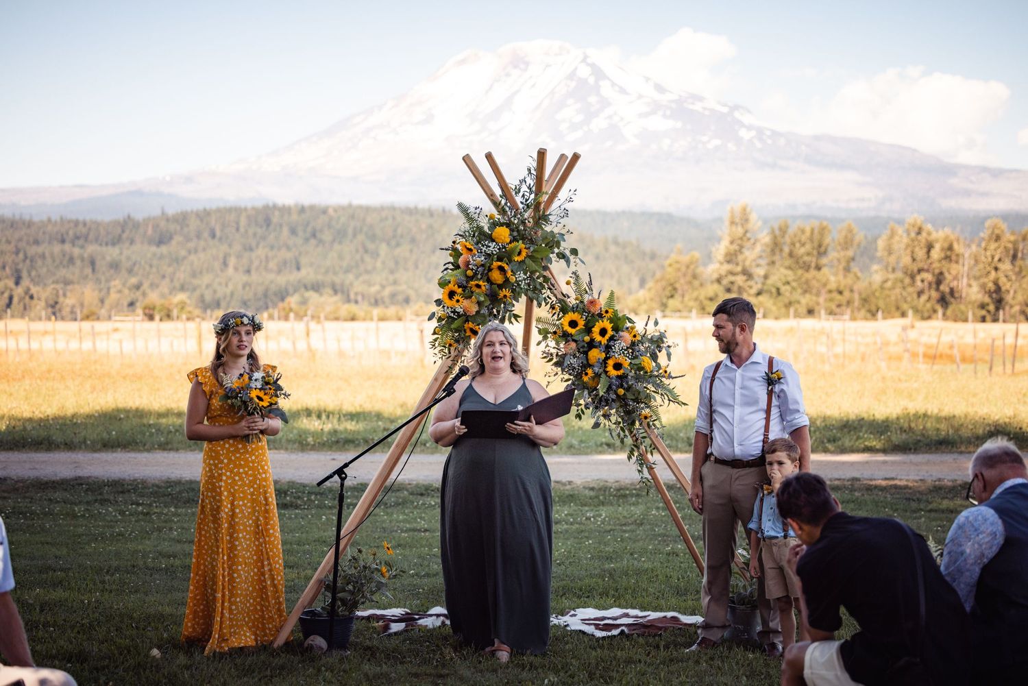 Outdoor wedding ceremony setup with wooden arch and floral decorations against mountain backdrop.