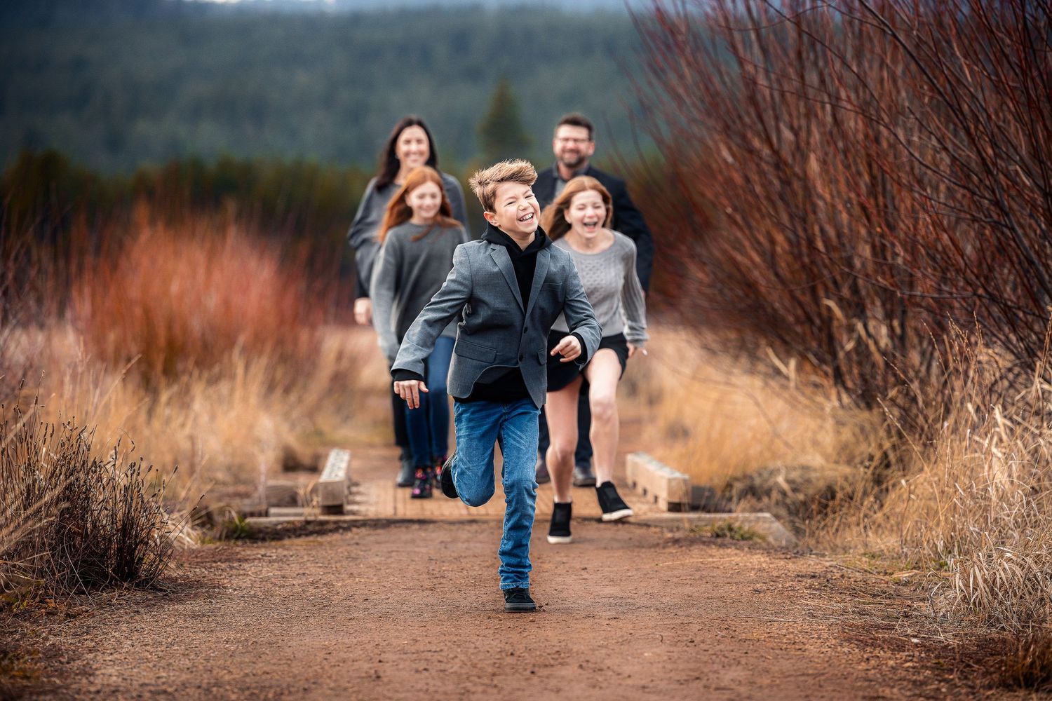 Family walking together on a dirt trail through autumn brush landscape.