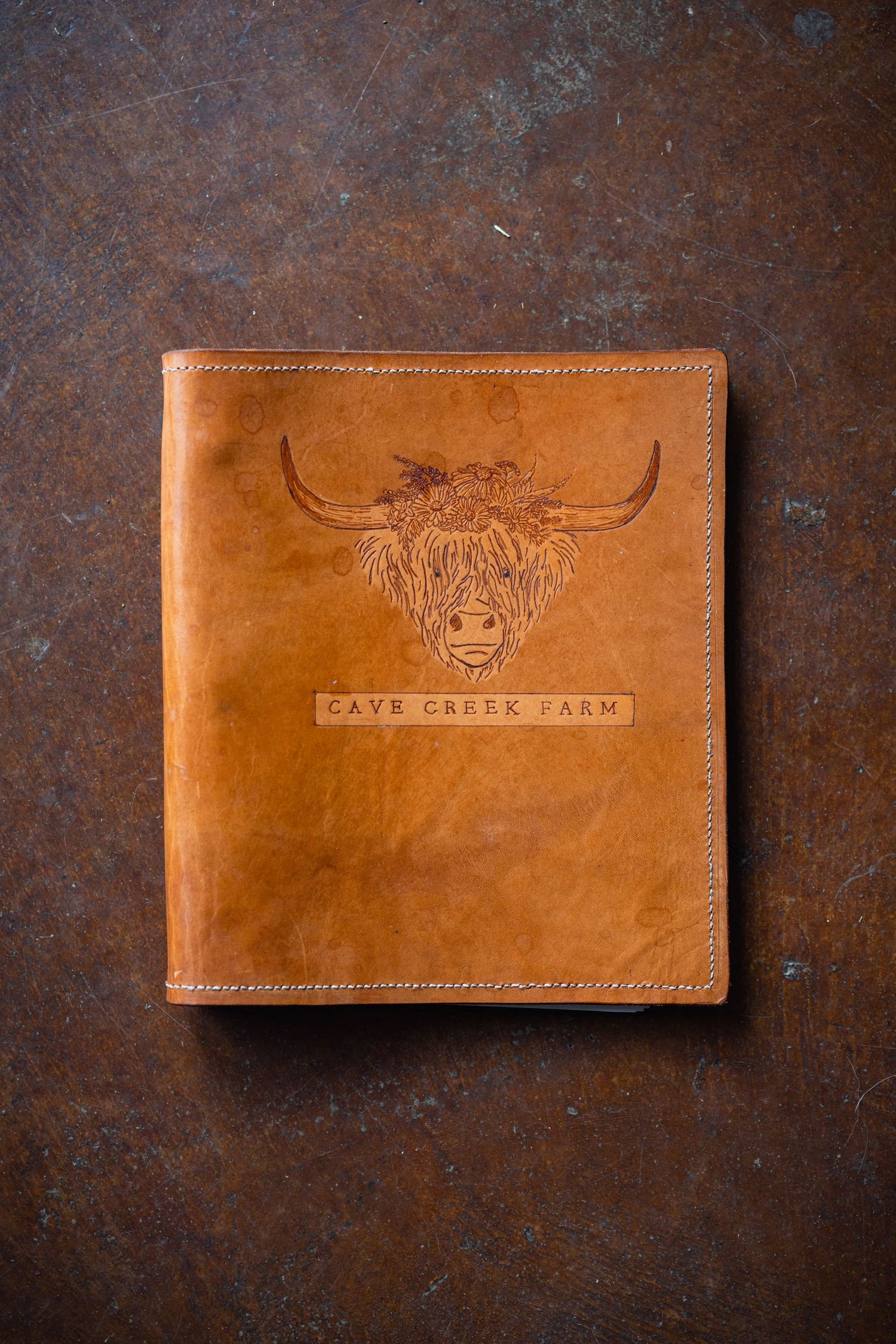 Tan leather wallet with embossed Highland cow logo and text 'Cave Creek Farm' on rustic brown background.