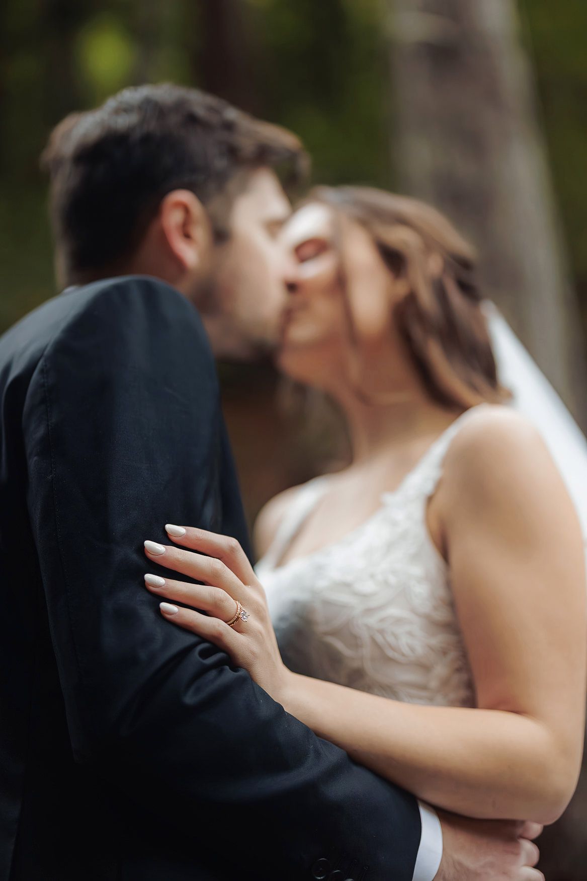 A tender wedding moment captured as newlyweds share a kiss outdoors with soft focus and romantic lighting.