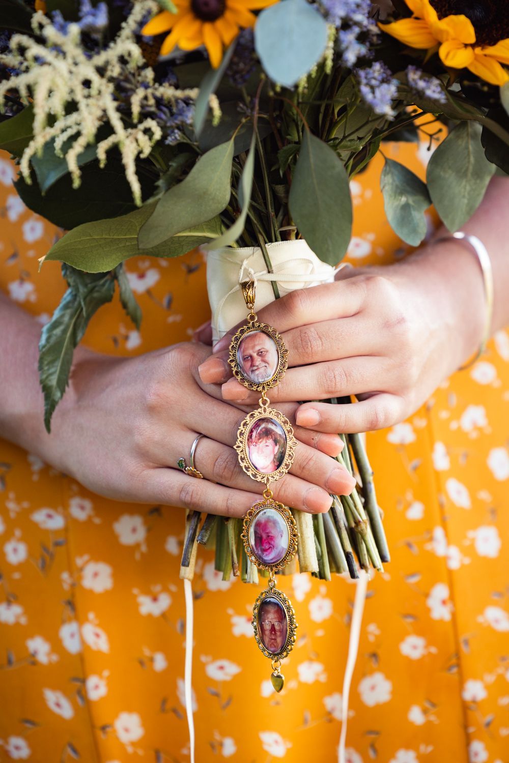 Hands holding a bouquet of sunflowers and greenery while wearing multiple antique cameo rings against an orange floral dress.