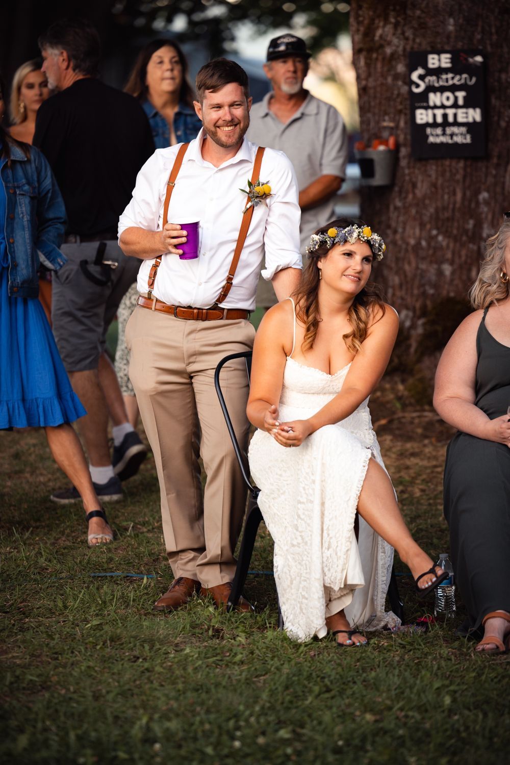 Guests at an outdoor wedding reception gather under trees with festive drinks and casual attire.
