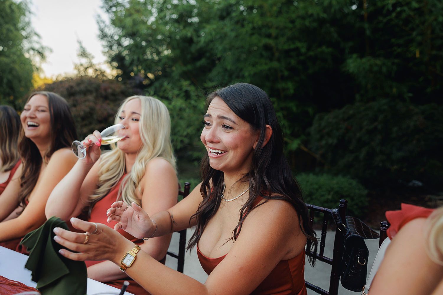 Wedding guests laugh and smile while watching entertainment during an outdoor evening celebration.