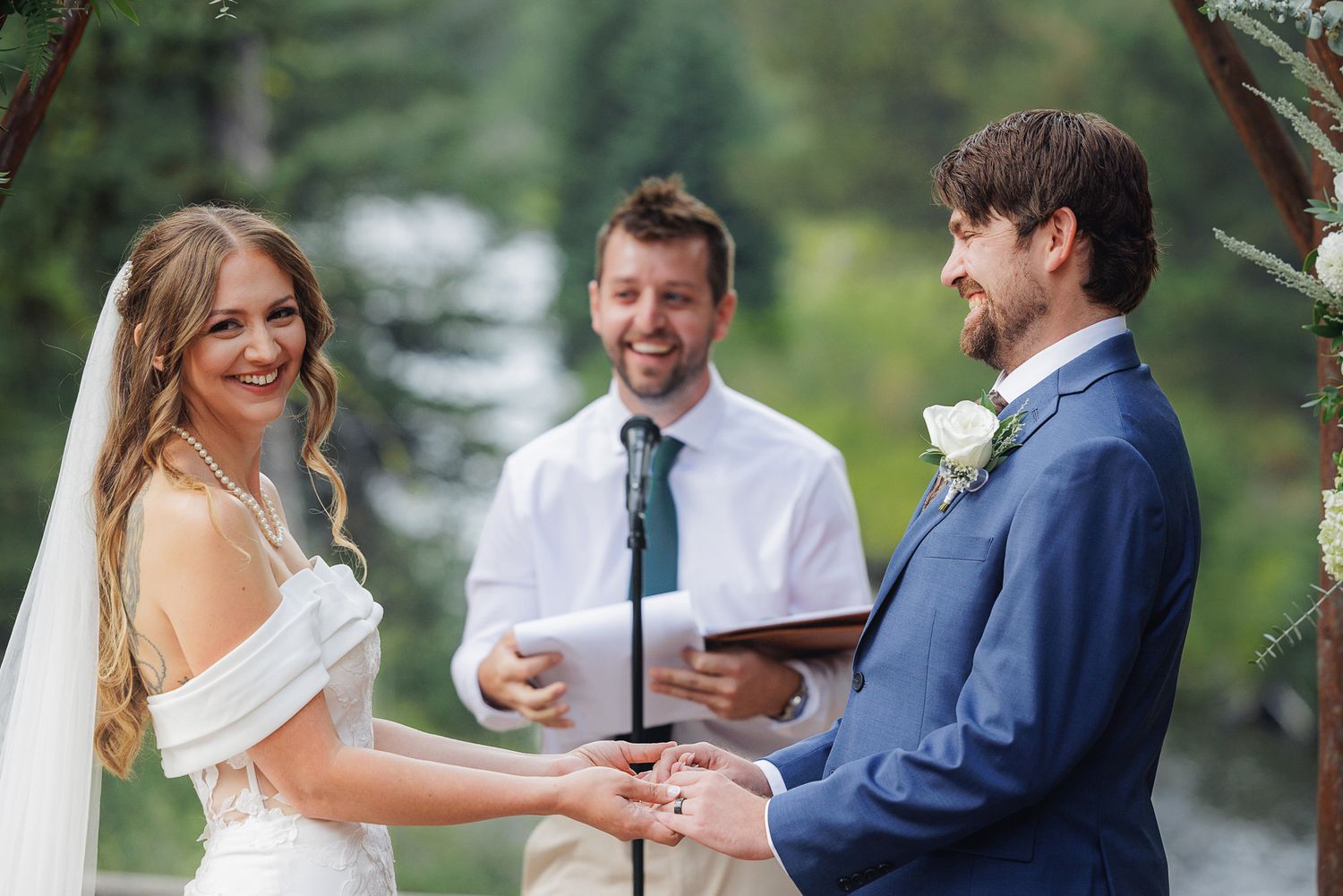 A couple holds hands during their outdoor wedding ceremony with an officiant standing between them.