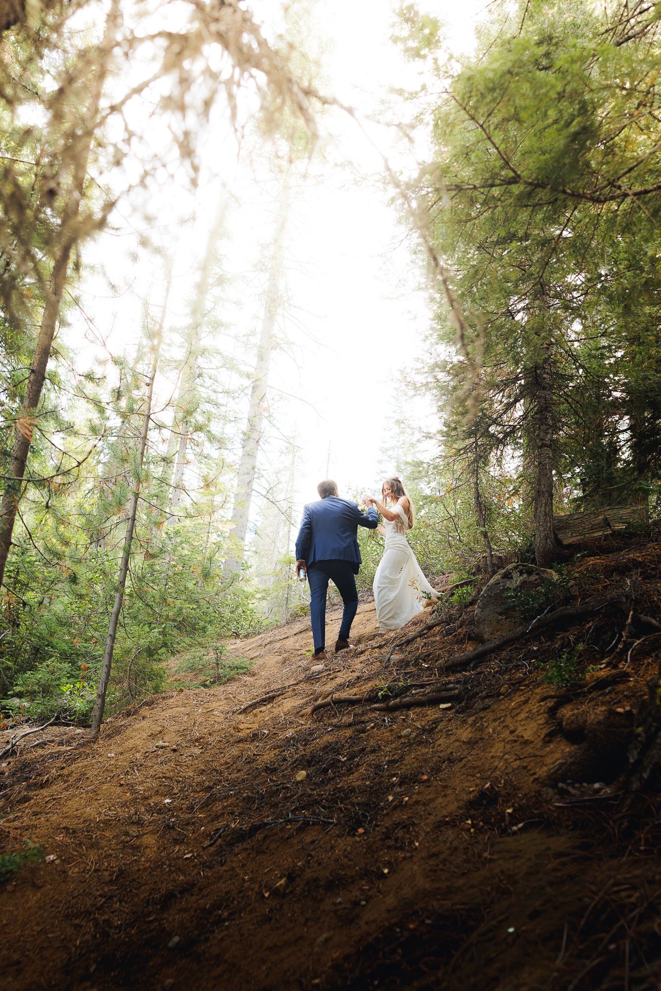 Two people hike up a steep dirt trail through a misty evergreen forest on a foggy morning.