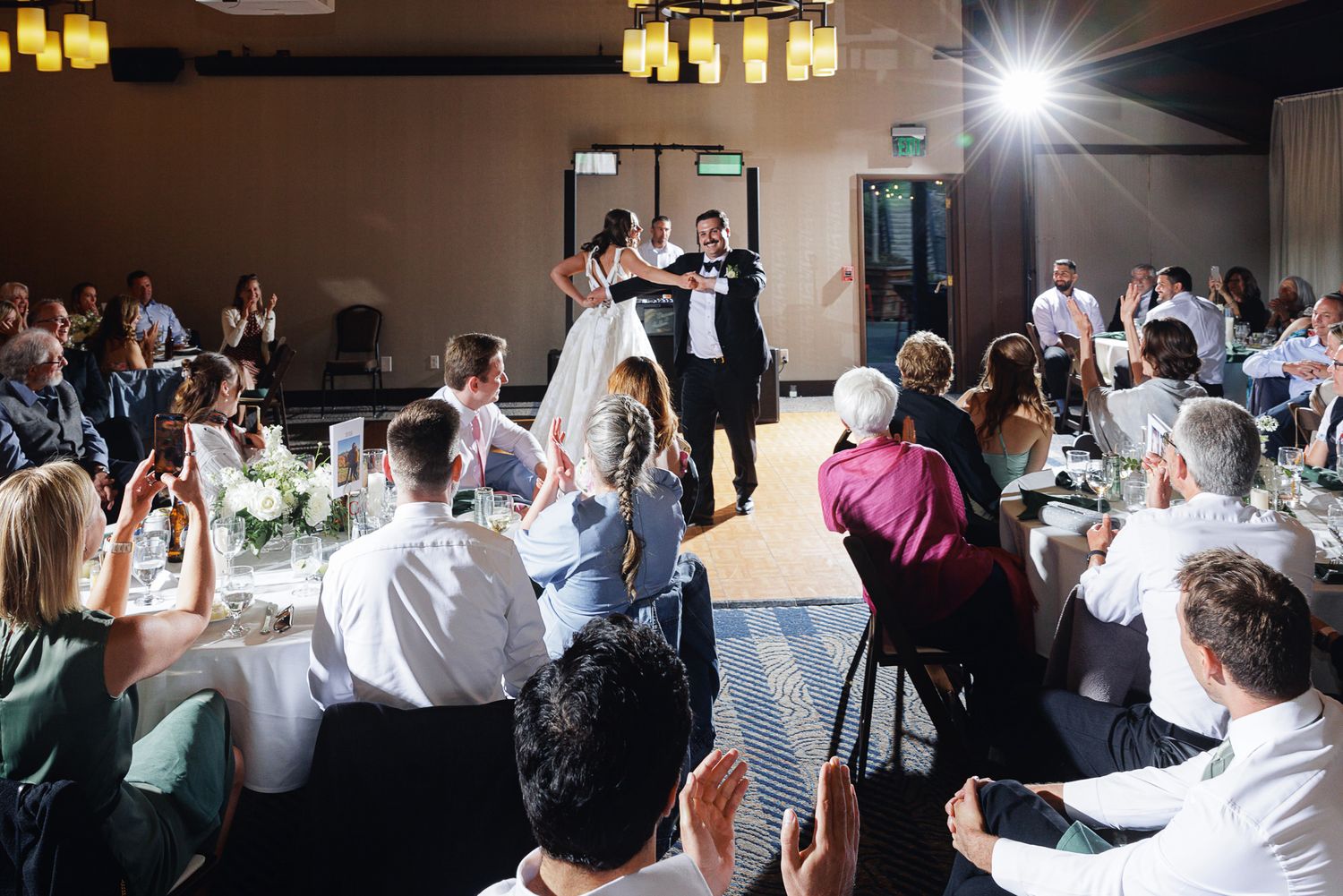Bride and groom make grand entrance at elegant wedding reception as guests cheer and applaud.