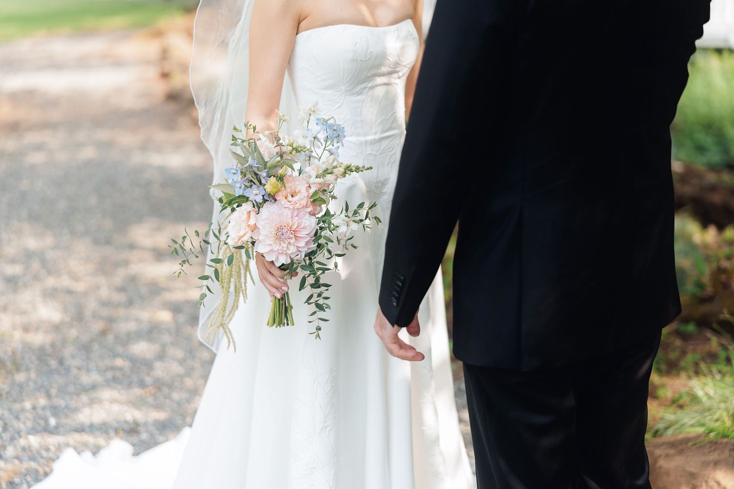 Bride and groom holding hands, bride carrying a pastel pink and blue floral wedding bouquet with greenery.