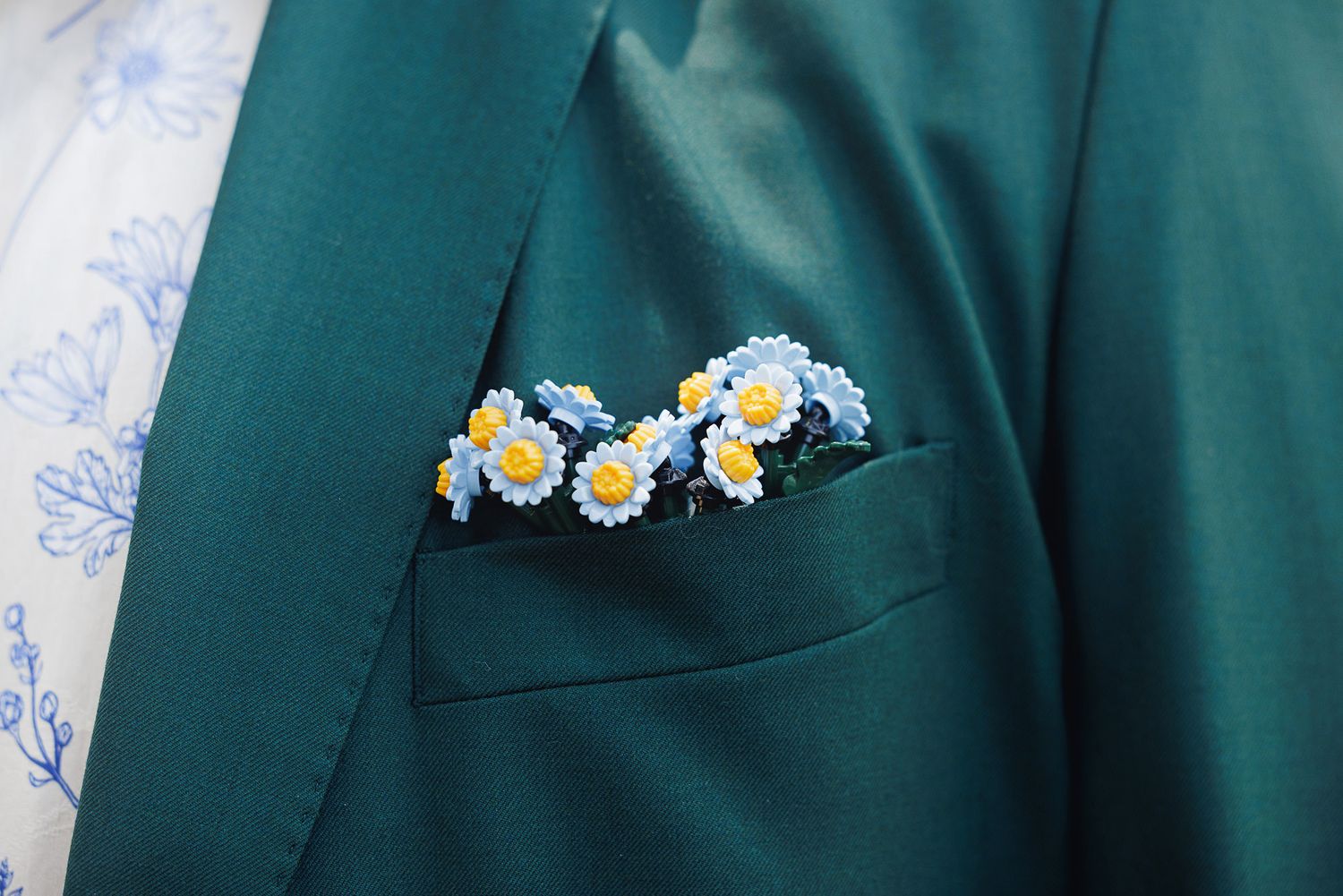 Teal suit jacket with a blue and white daisy floral pocket square arrangement.