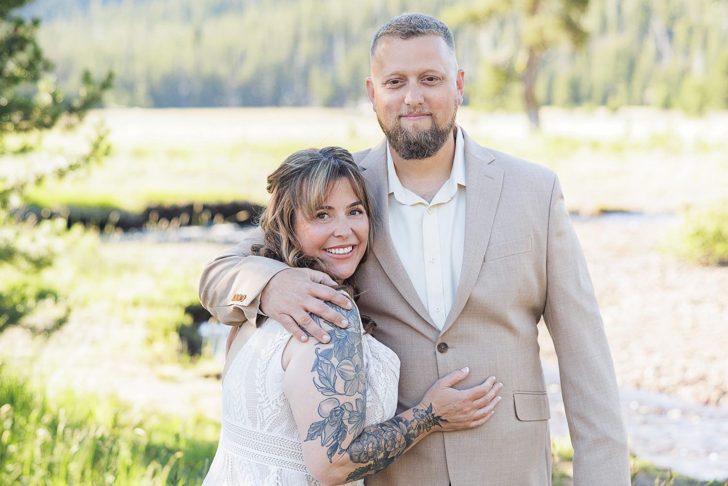 A couple embrace in casual attire against a scenic mountain landscape backdrop.