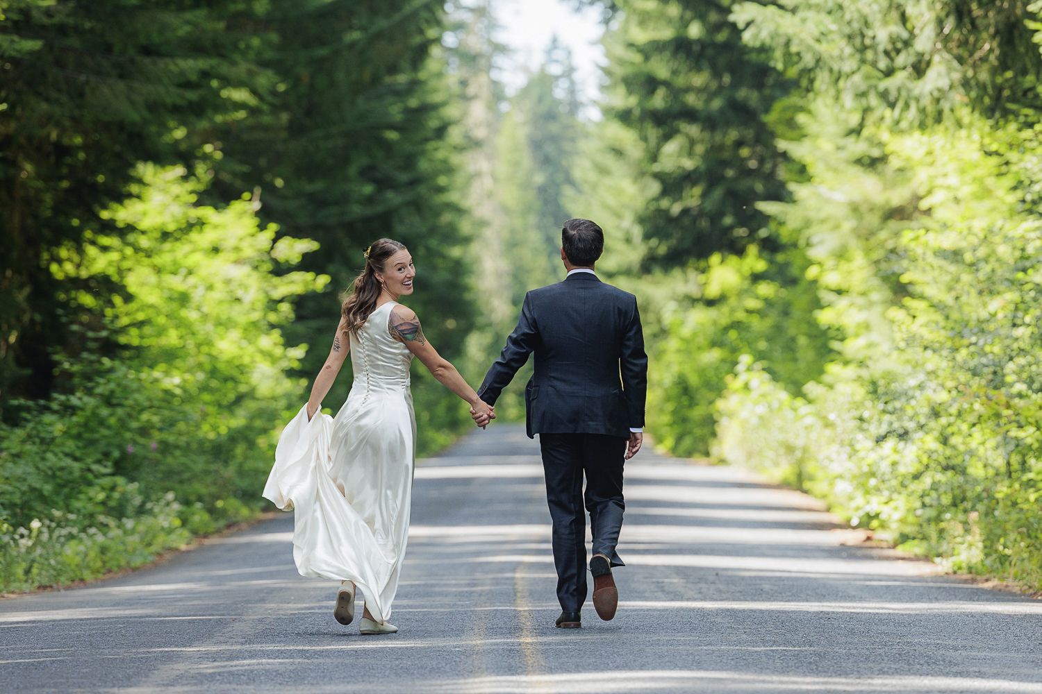 Couple walking together on a tree-lined mountain road surrounded by evergreen forest.
