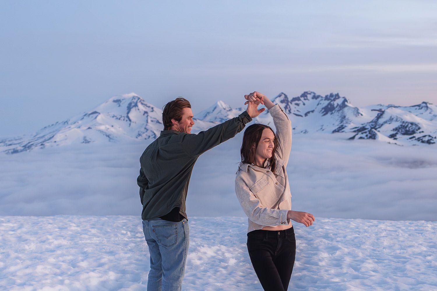 Two people dance together on a snowy mountain peak with a scenic winter landscape in the background.