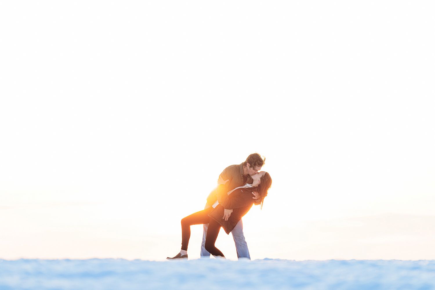 A silhouetted couple embraces during a golden sunset on a snowy landscape.