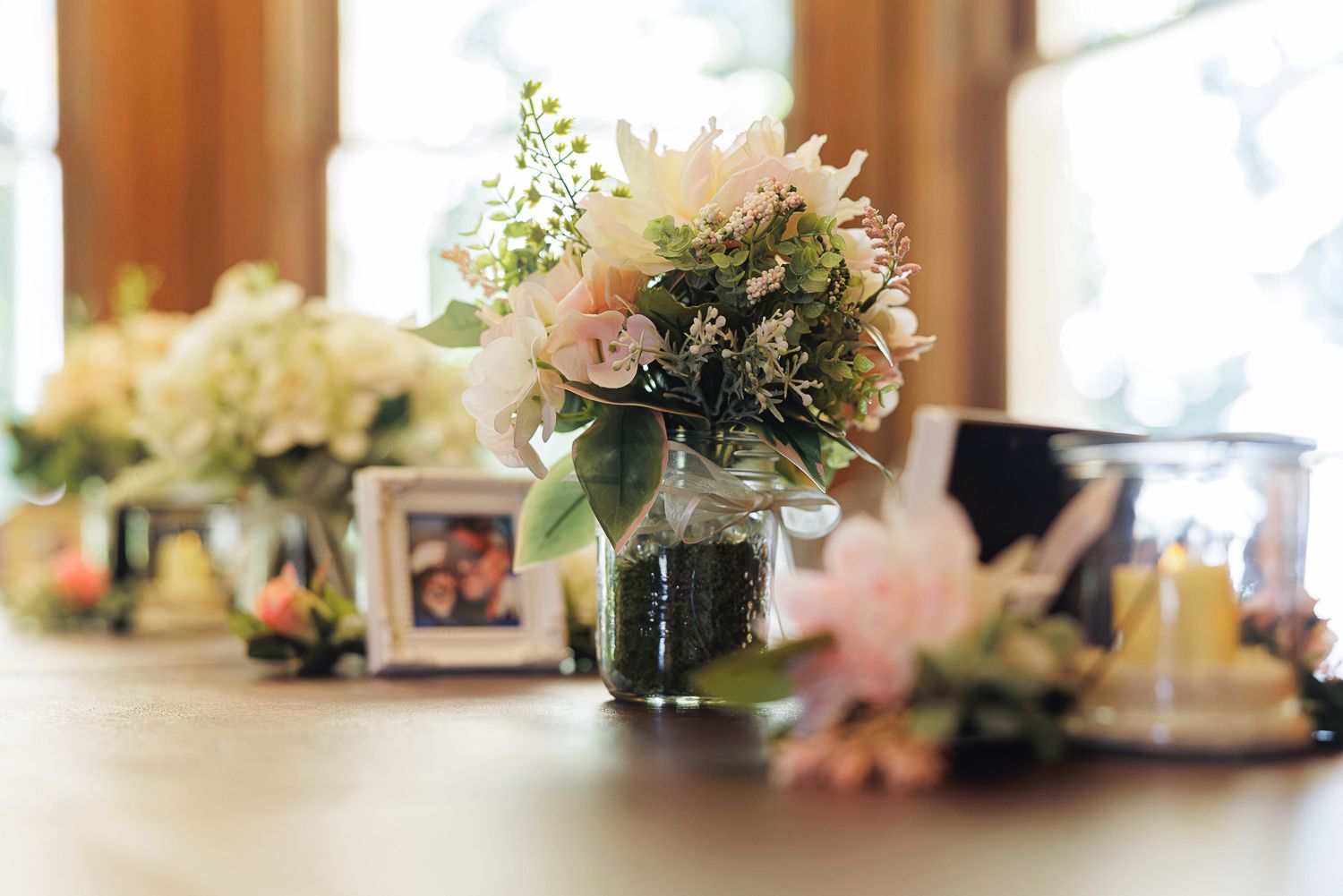 Row of elegant floral centerpieces with white and pink blooms arranged on a sunlit table.