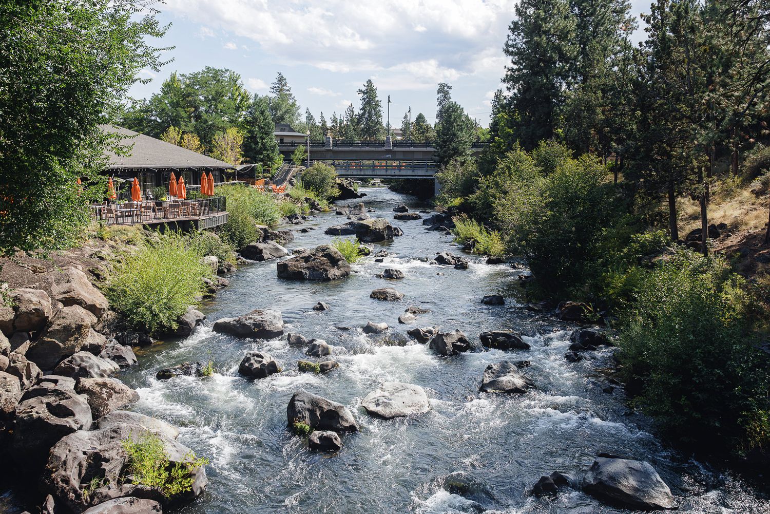 A scenic river flows through rocky terrain surrounded by evergreen trees and natural boulders in a mountain landscape.
