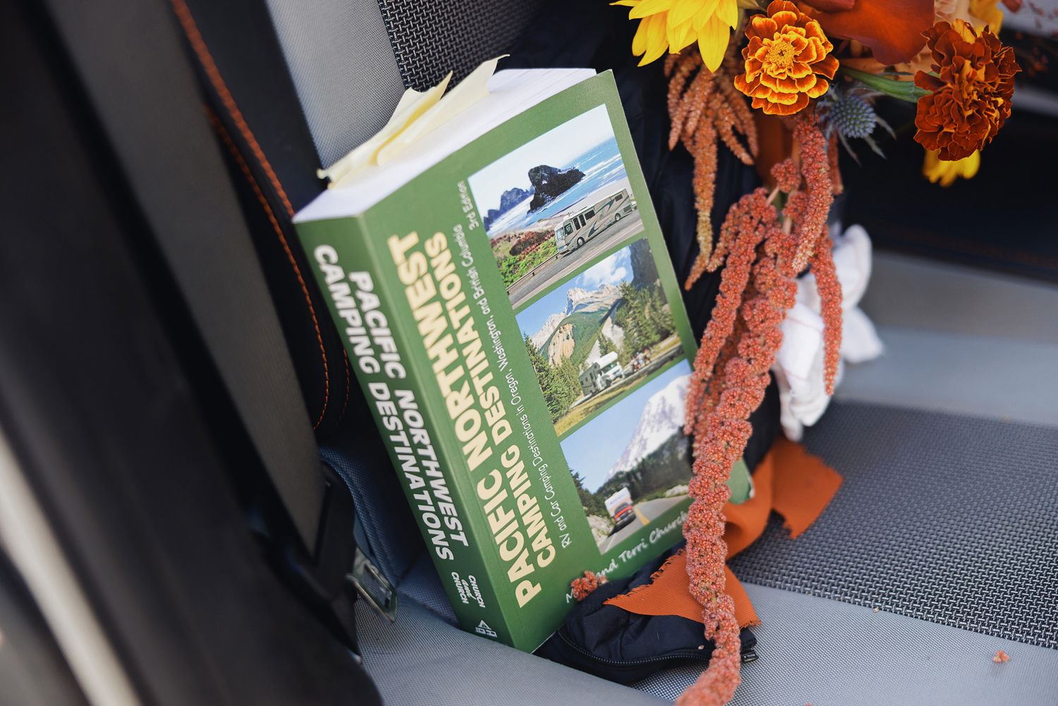 Pacific Northwest camping destinations guidebook with an open page rests on a seat beside orange autumn flowers and amaranth.