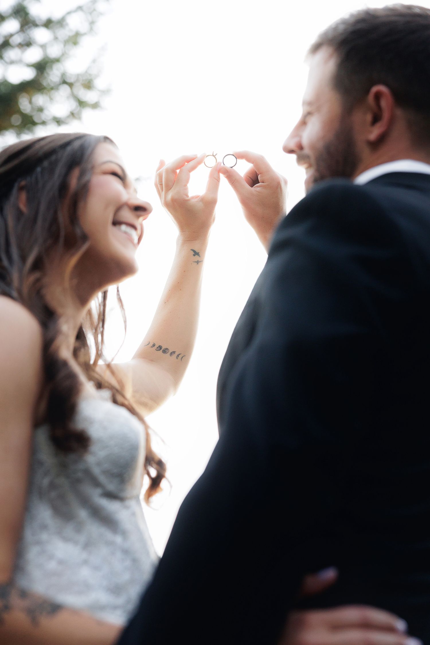 Smiling bride and groom holding up wedding rings together on their wedding day.