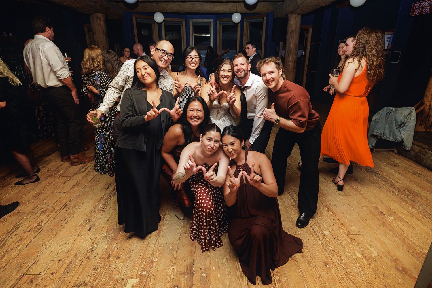 Group of friends posing and smiling on a wooden dance floor at a festive wedding reception party.