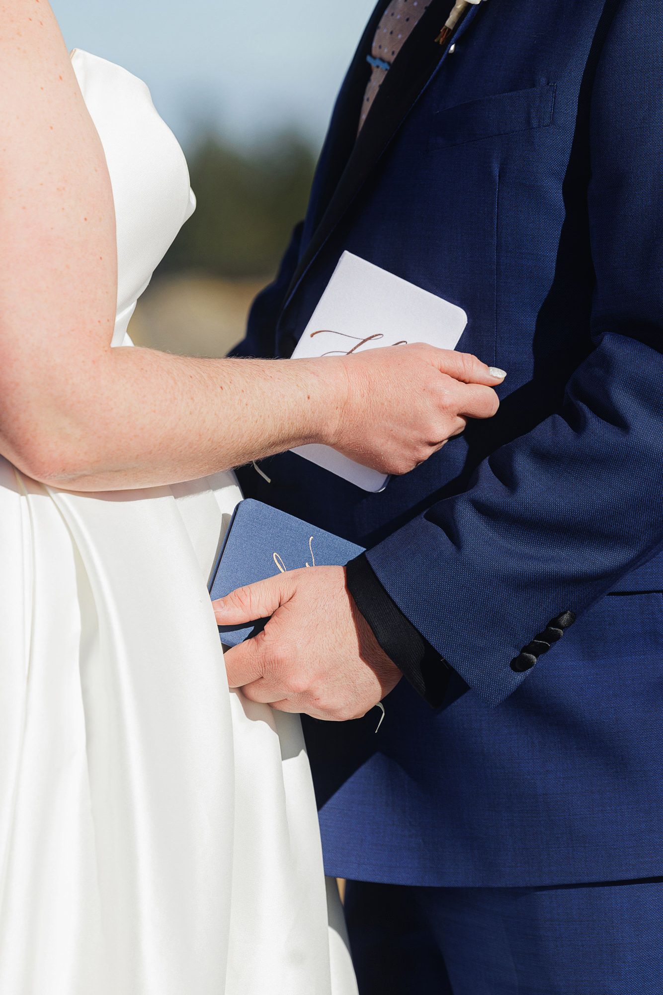 Close-up of bride and groom exchanging rings during wedding ceremony with hands in navy suit and white dress.