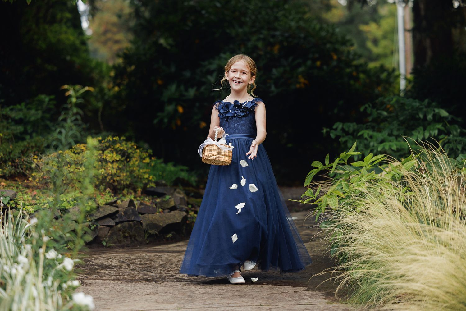A person in a navy blue dress sits on a rustic wooden bench surrounded by lush garden foliage.