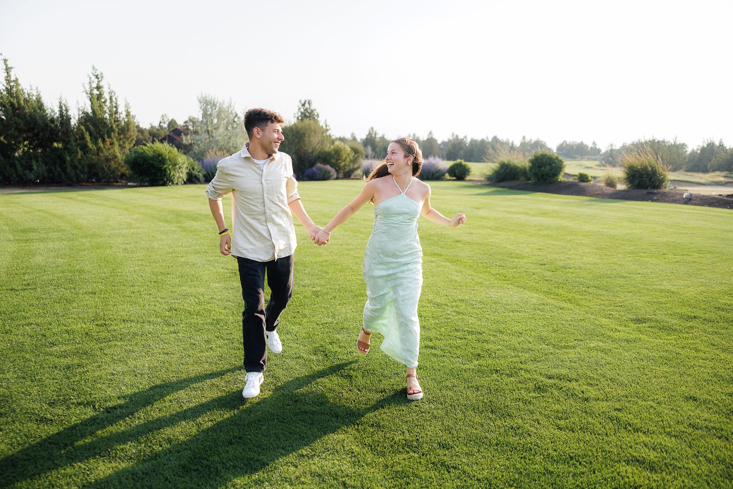 Happy couple holding hands and walking on lush green grass outdoors on a sunny day.