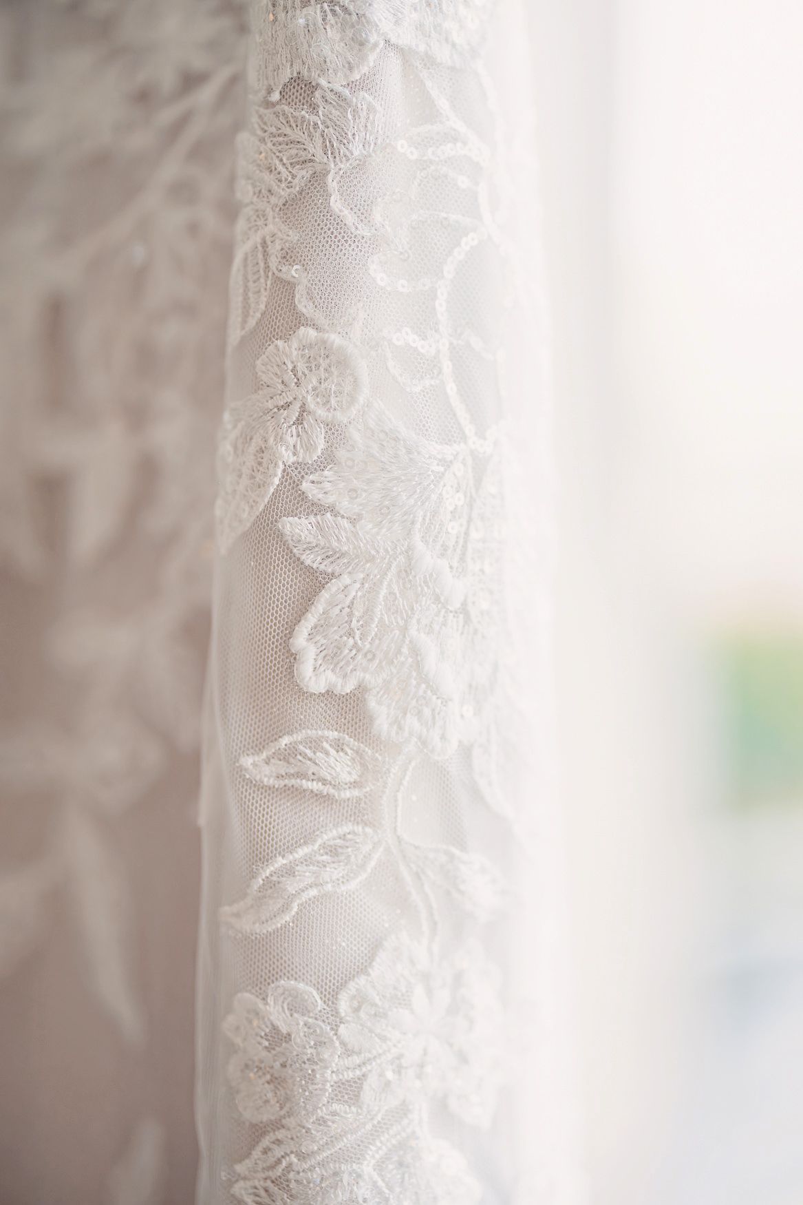 Delicate white lace fabric with intricate floral embroidery pattern shown in soft focus detail.