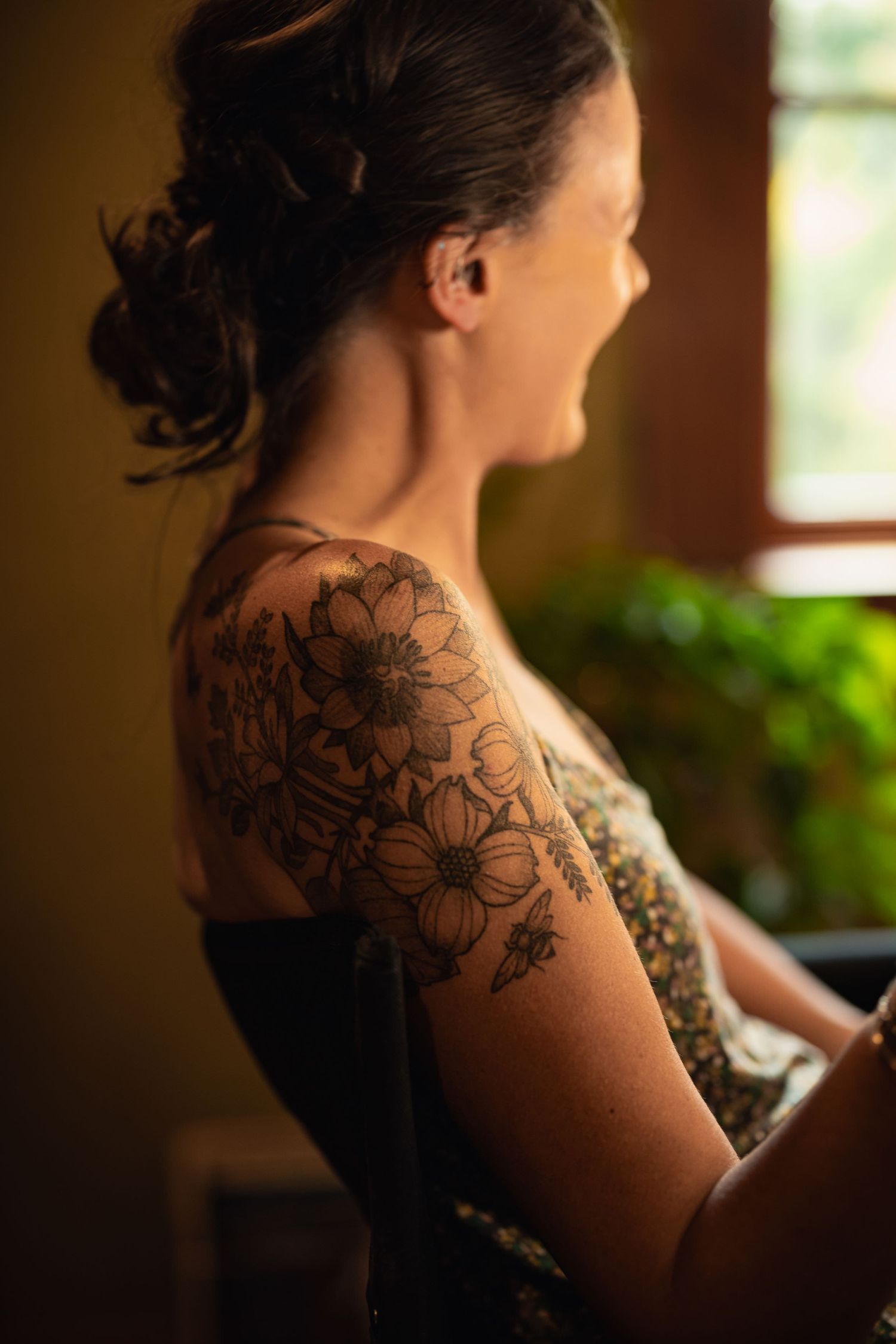 Side view of a floral tattoo design featuring dark linework daisies on a shoulder in warm lighting.