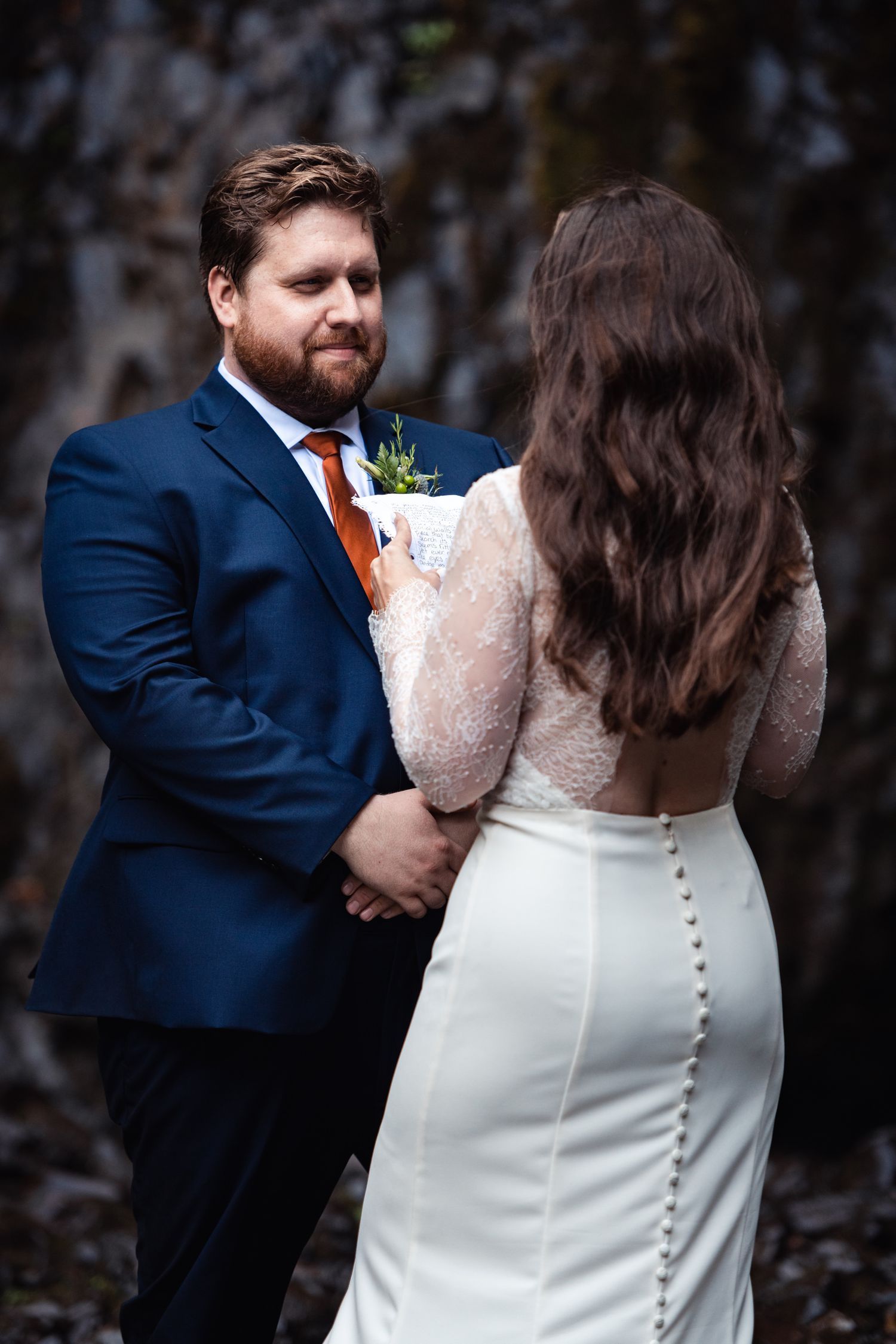 A bride and groom share a tender moment at their wedding, with her wearing a fitted white gown and him in a navy suit.