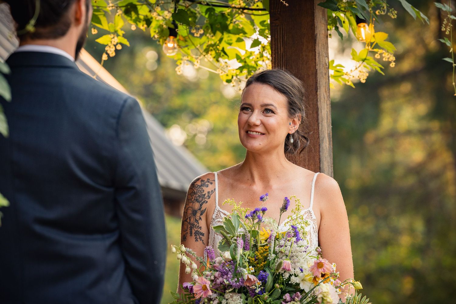 A ceremony takes place under wooden beams with sunlit leaves overhead.