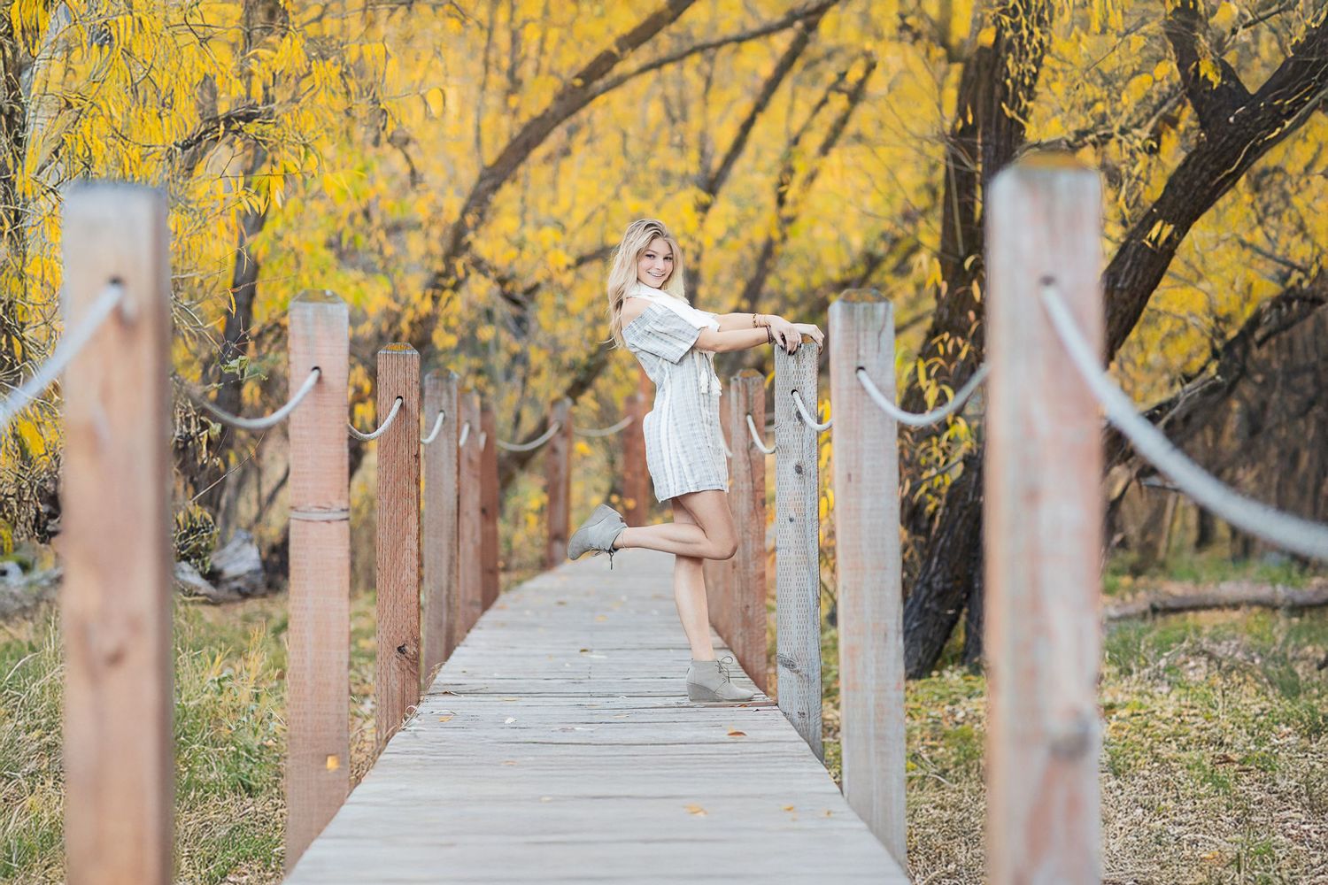 A wooden boardwalk through yellow autumn trees with someone leaping joyfully in the middle.