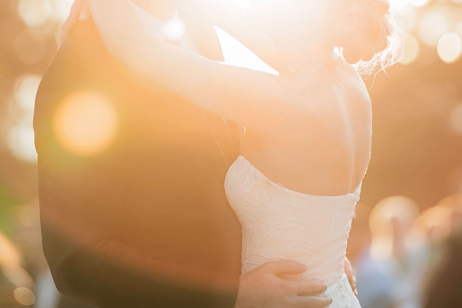 Couple sharing a romantic first dance bathed in golden sunset light at an outdoor wedding reception.