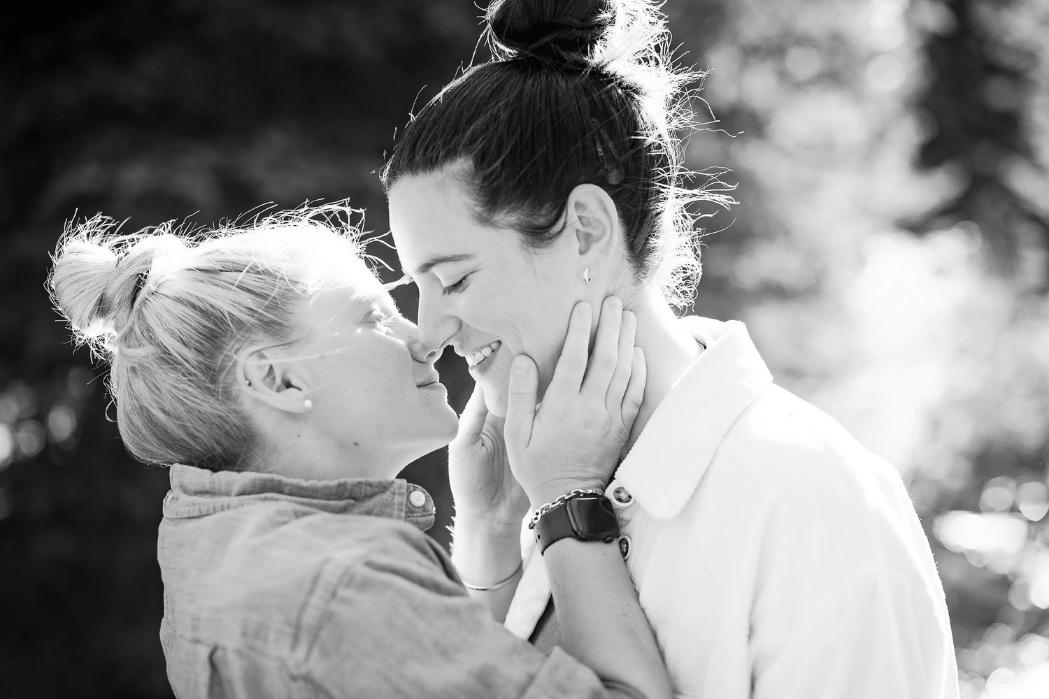 A tender black and white portrait showing a loving moment between two people sharing an intimate embrace outdoors.