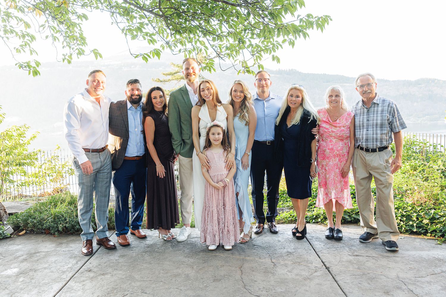 A large family group poses together outdoors on a patio with scenic mountain views during a special occasion.
