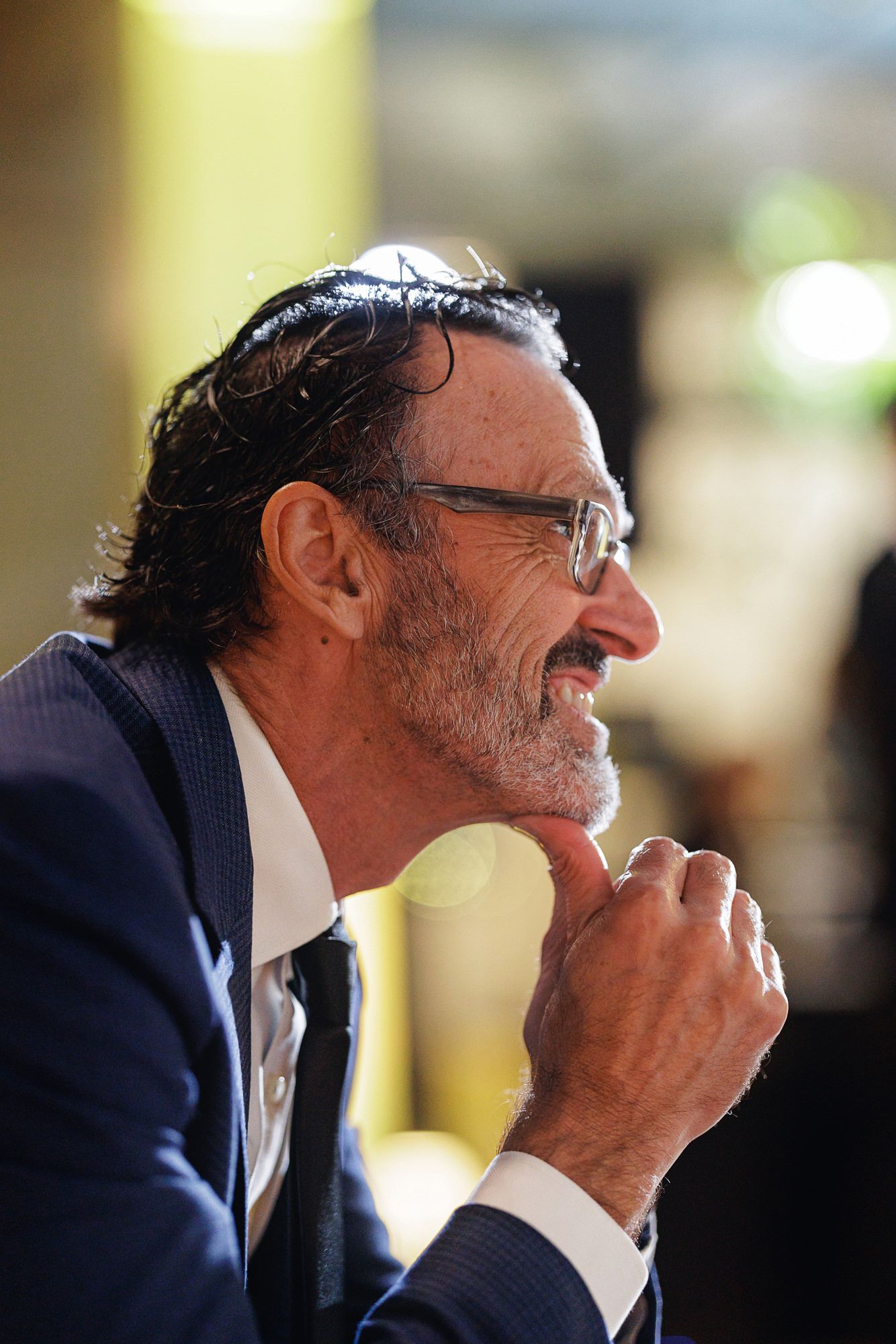 Smiling middle-aged man with glasses and salt-pepper hair wearing a navy suit at a formal event.