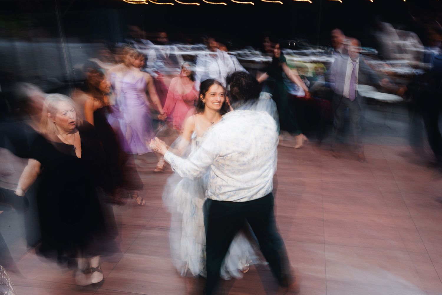 Bride and groom share a joyful first dance surrounded by guests at a lively wedding reception.