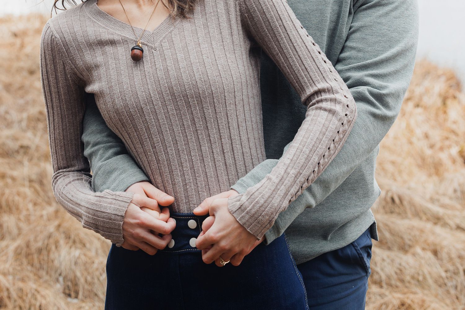 A couple wearing cozy sweaters embraces in a golden field during autumn.