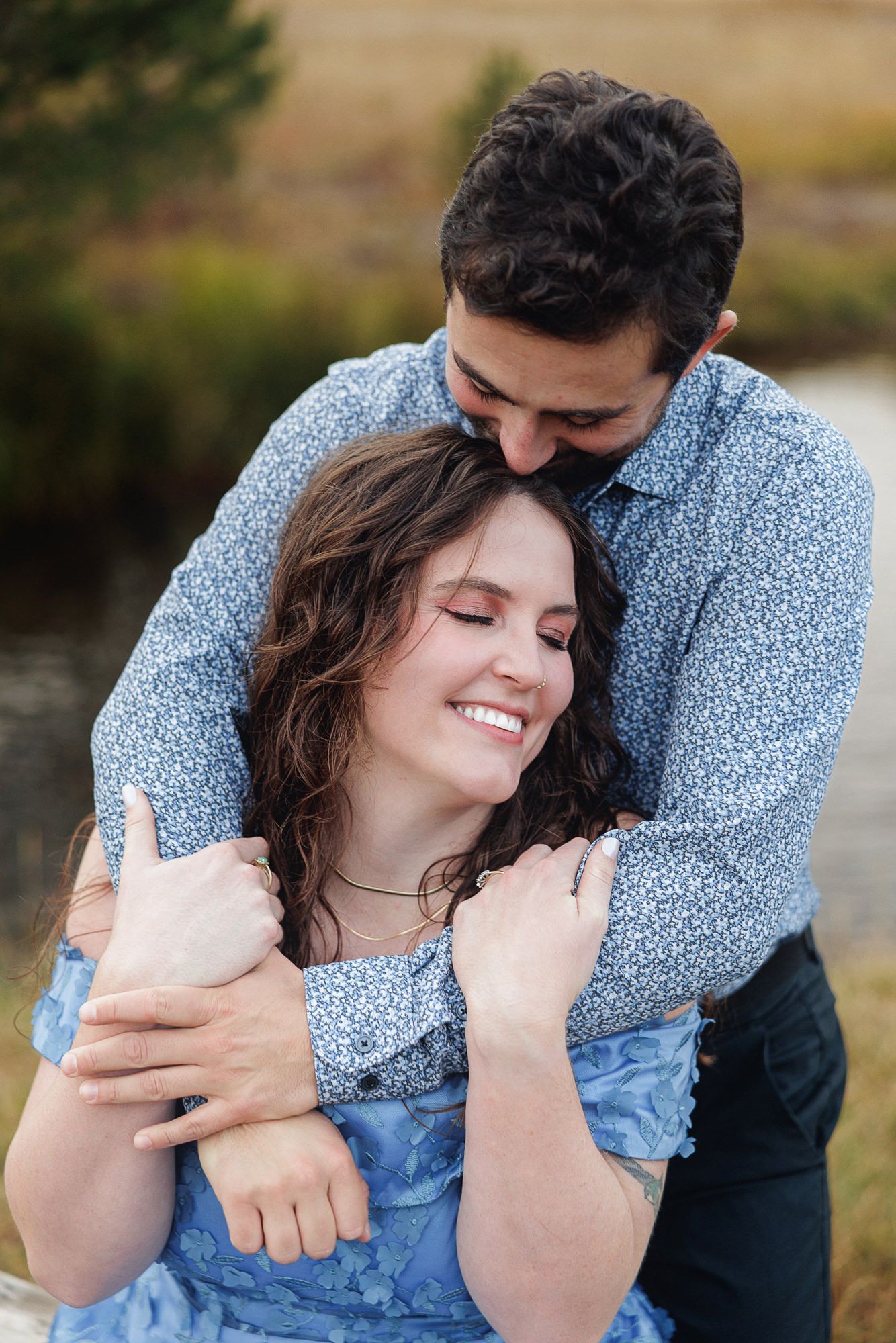 A romantic outdoor portrait of a couple embracing, with the person in blue denim and floral print showing a joyful smile.