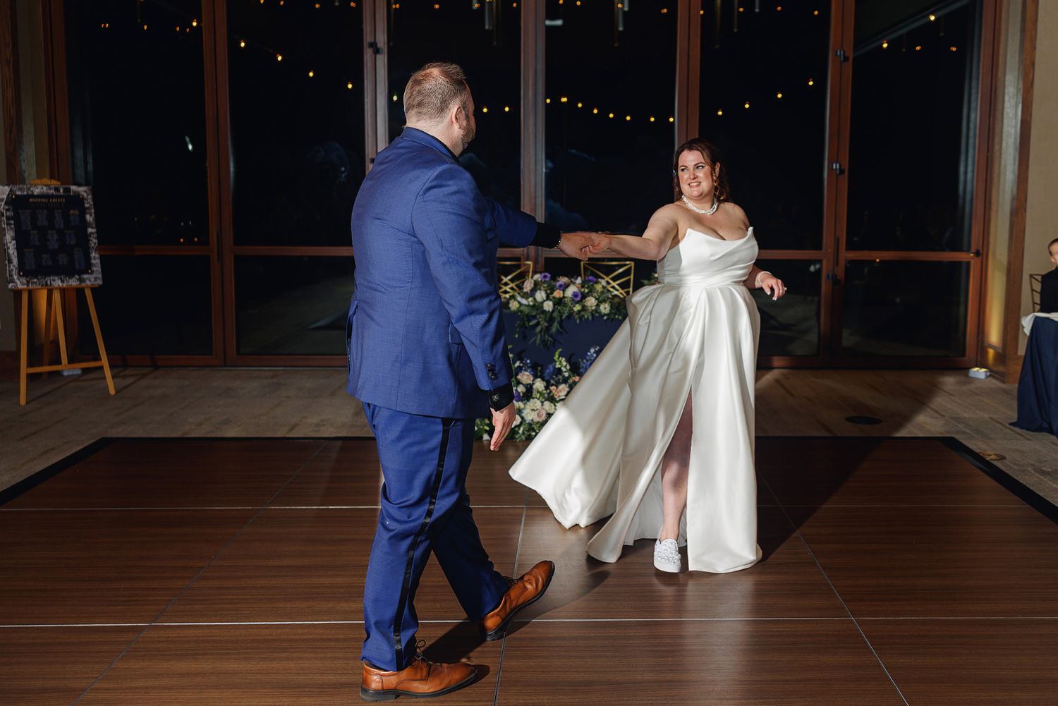 A couple in wedding attire dances together on a wooden floor during their reception celebration.