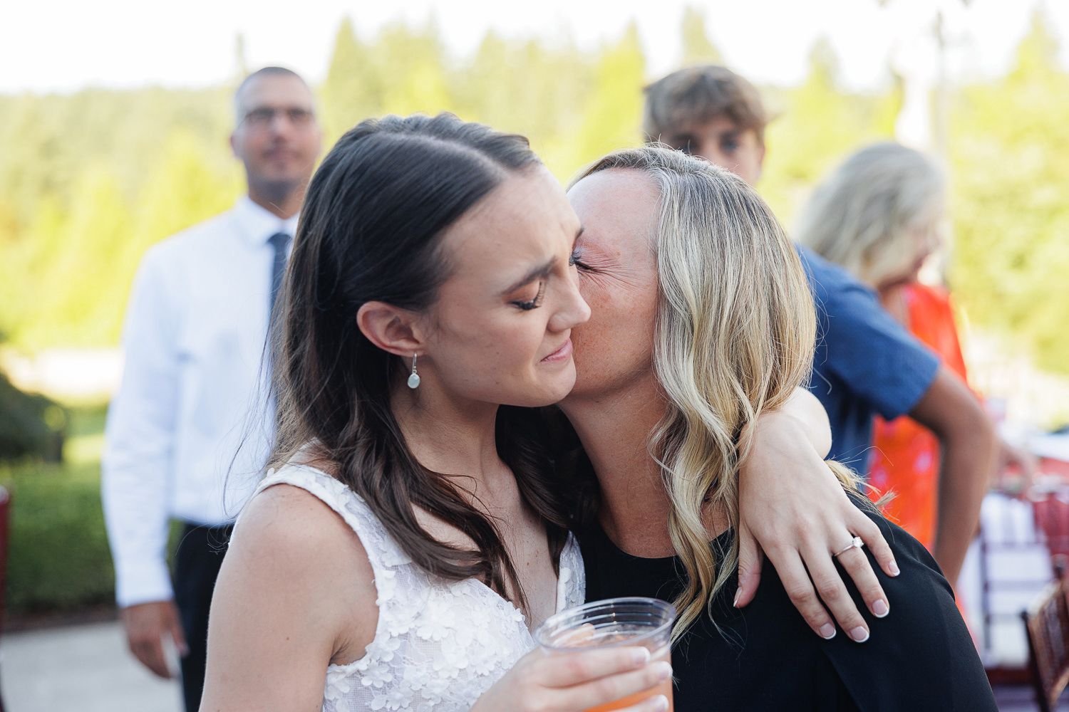 Two people share a tender kiss outdoors during what appears to be a wedding celebration.