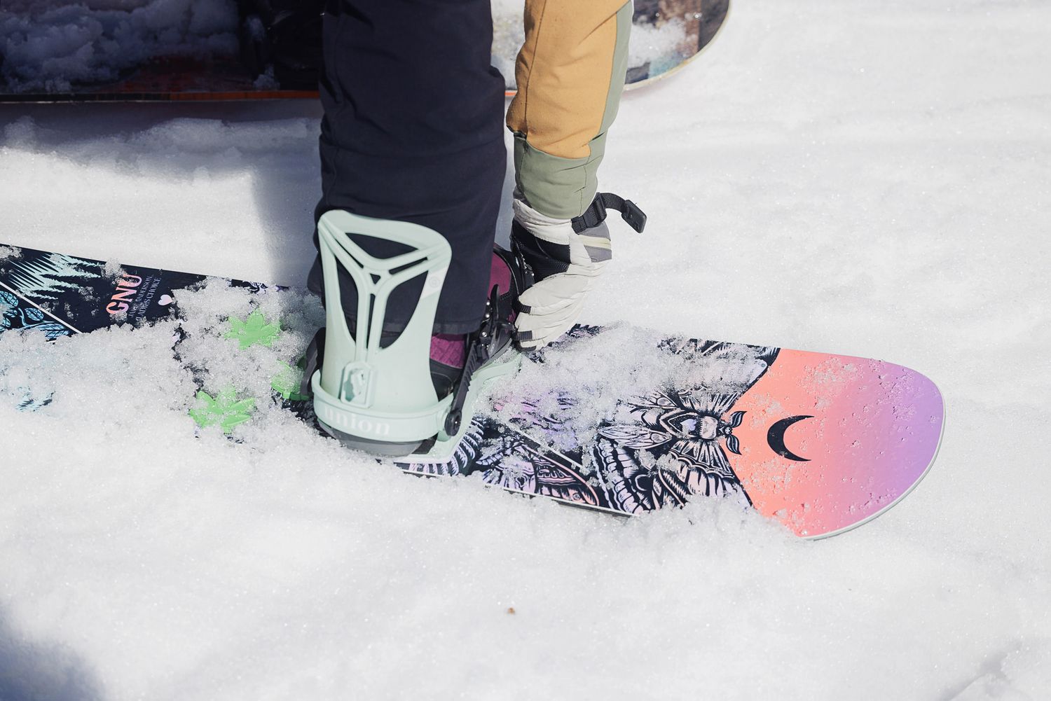 A person's snowboard and boot on a snowy surface, with a ski lift visible in the background.