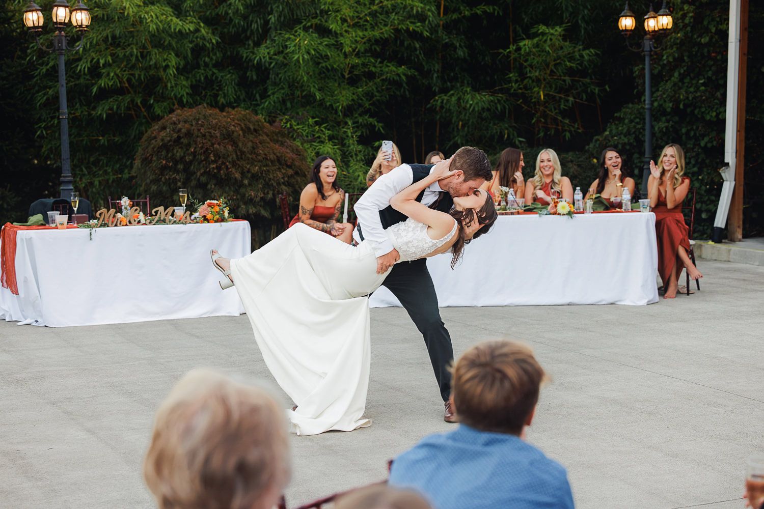 Wedding celebration with guests dancing and celebrating on an outdoor patio under string lights.