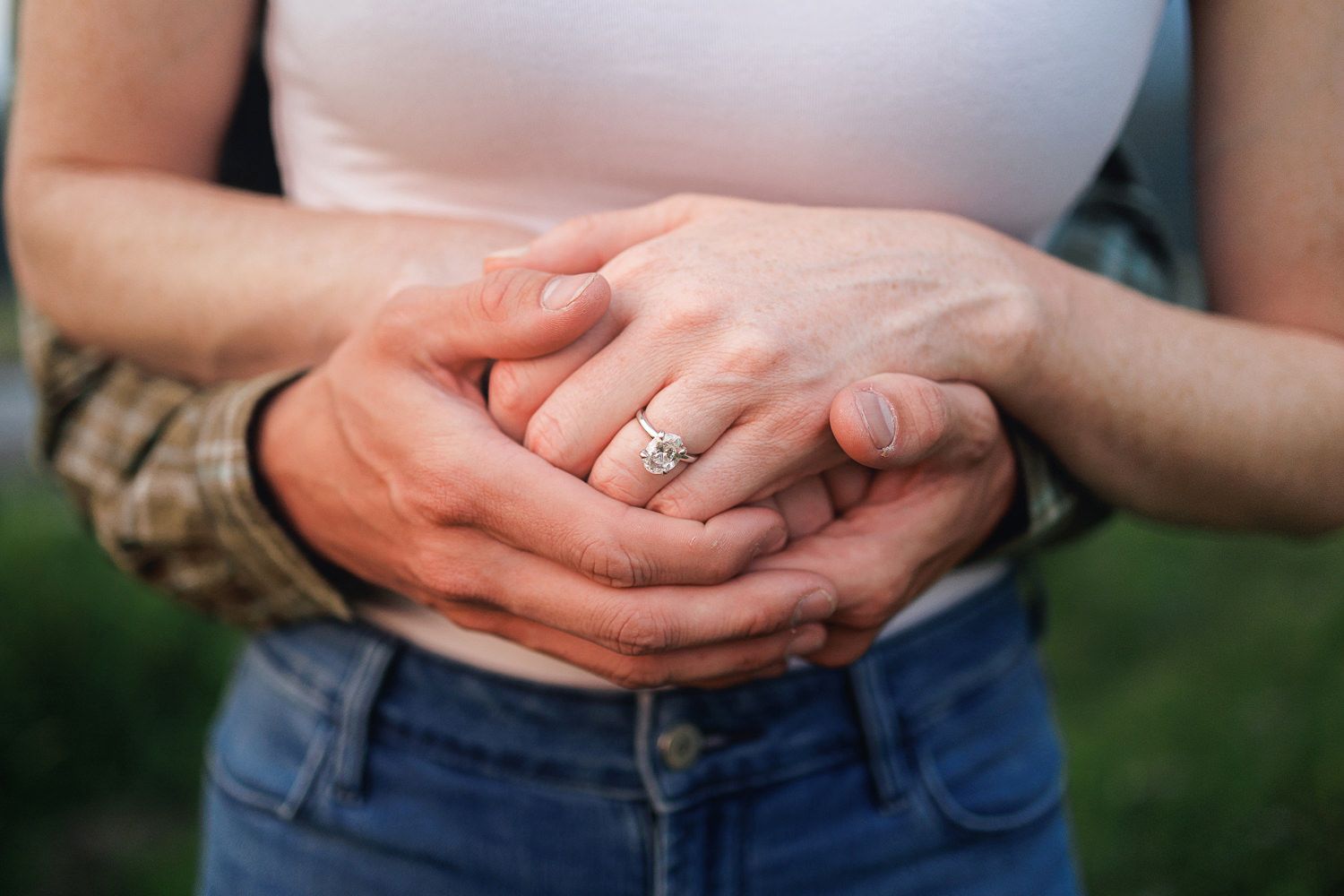 Closeup shot of hands wearing a silver ring outdoors with sunlight filtering through green nature background.