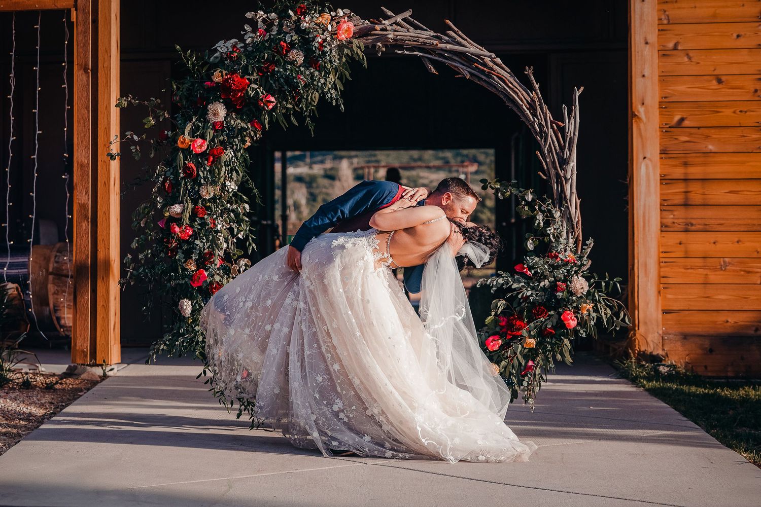 A romantic moment under a floral arch decorated with red blooms.