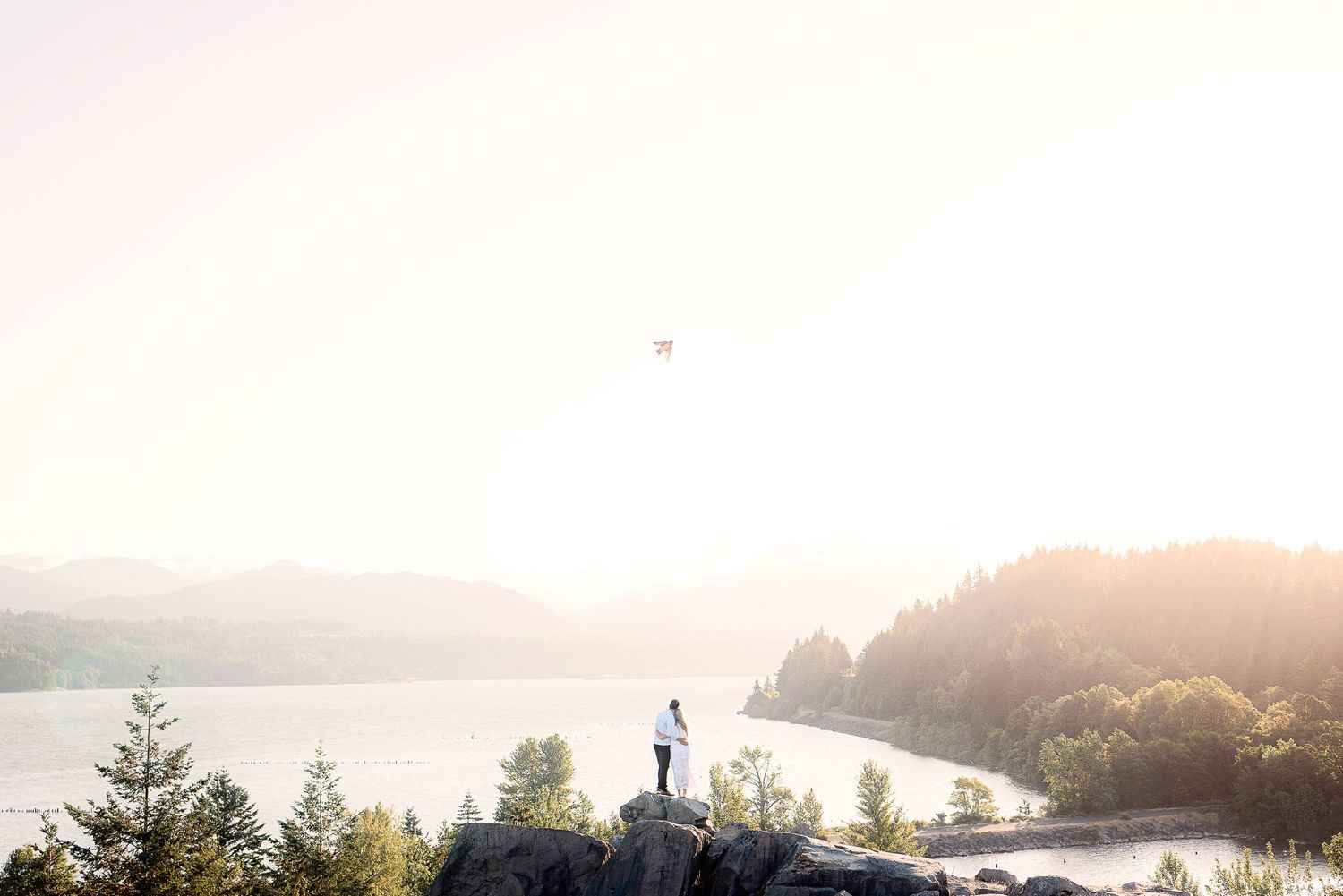 Silhouette of figure standing on cliff overlooking misty lake and mountains at sunset.