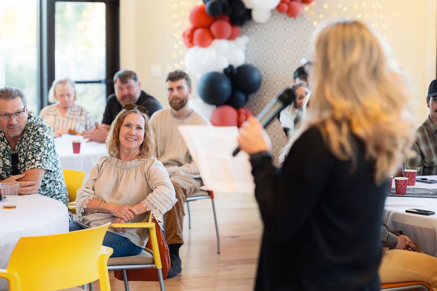 Attendees seated at tables during a presentation with black and orange balloon decorations.