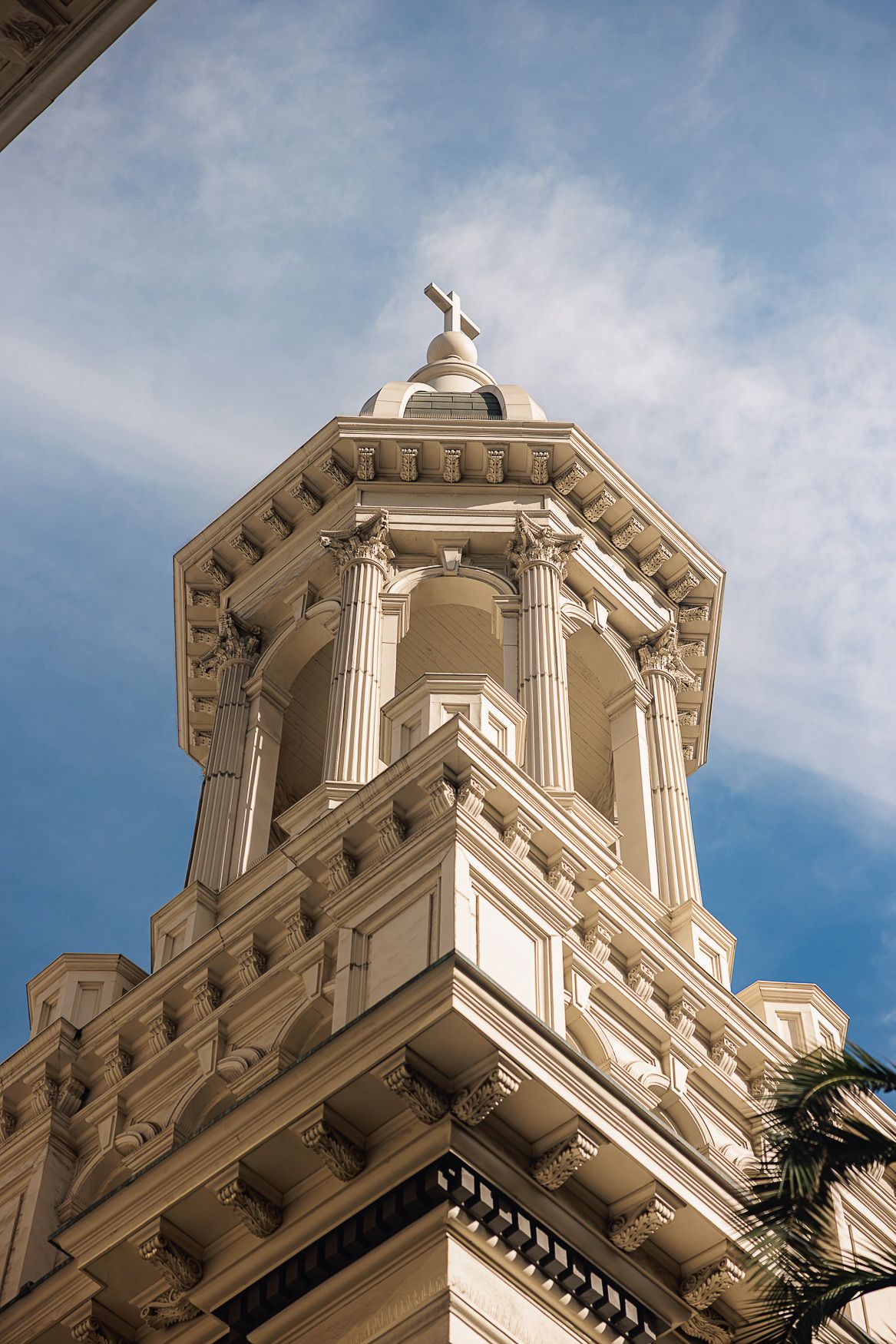 Ornate white church steeple with classical columns and architectural details rises against a blue sky with wispy clouds.