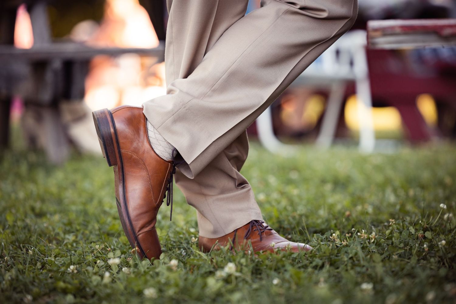 Close-up of brown leather dress shoes with khaki pants on grass, showing polished footwear details.